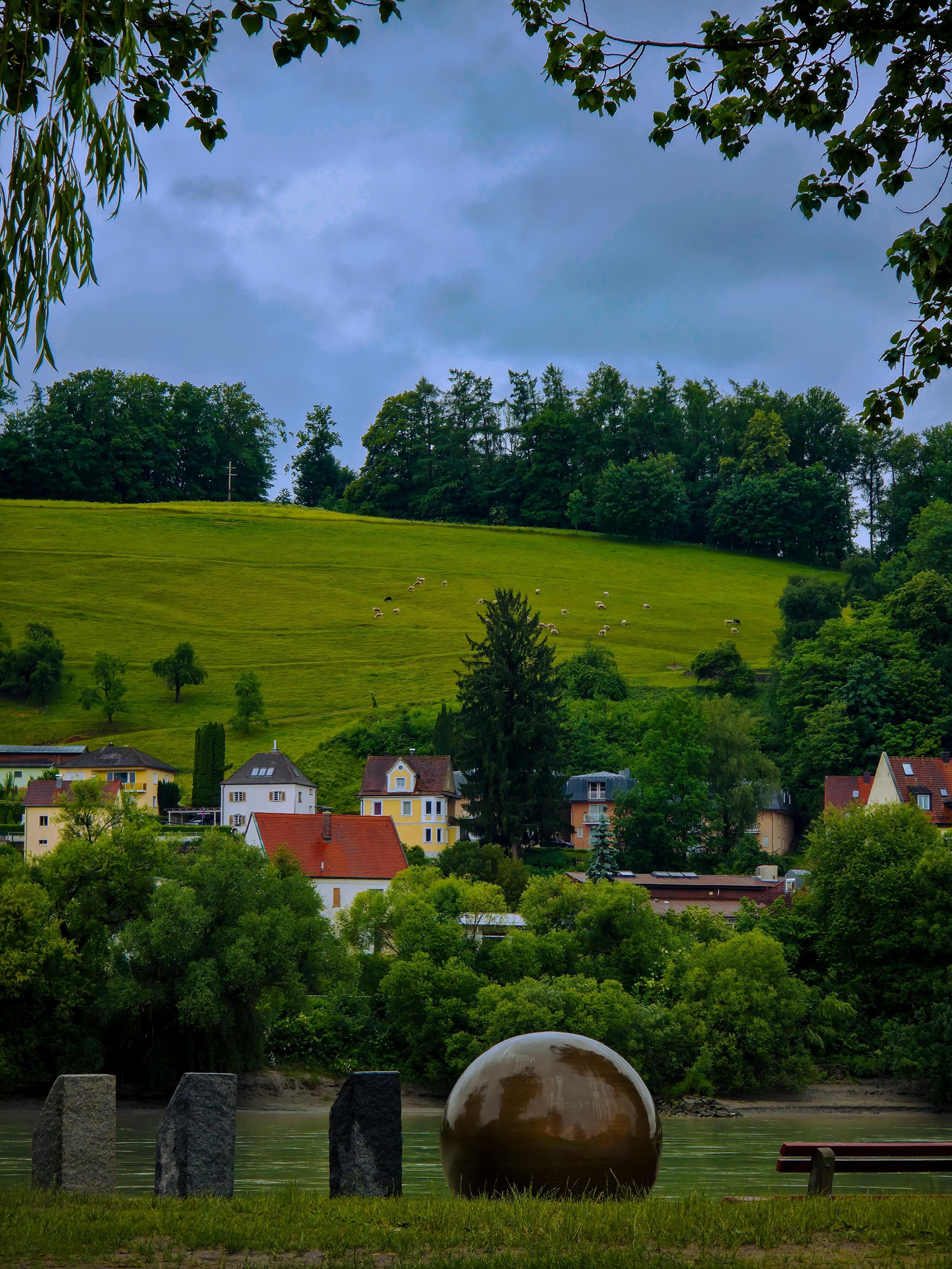 A scenic view of a winding mountain road cutting through lush green valleys under a dynamic, cloudy sky.